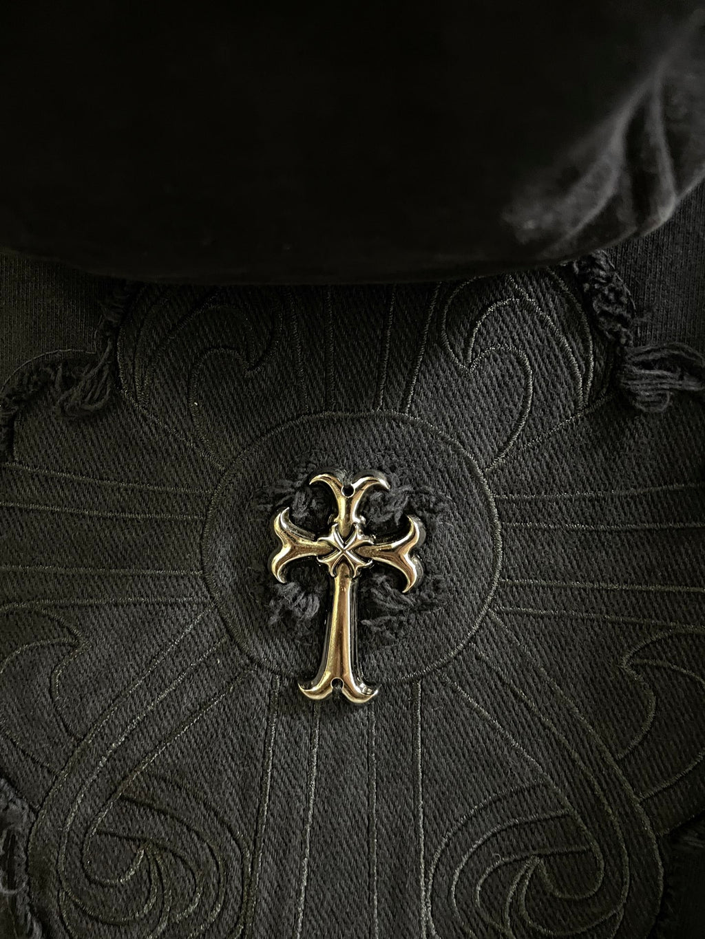 Close-up of dark embroidered cross emblem on patterned fabric center panel