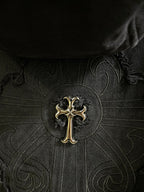 Close-up of dark embroidered cross emblem on patterned fabric center panel