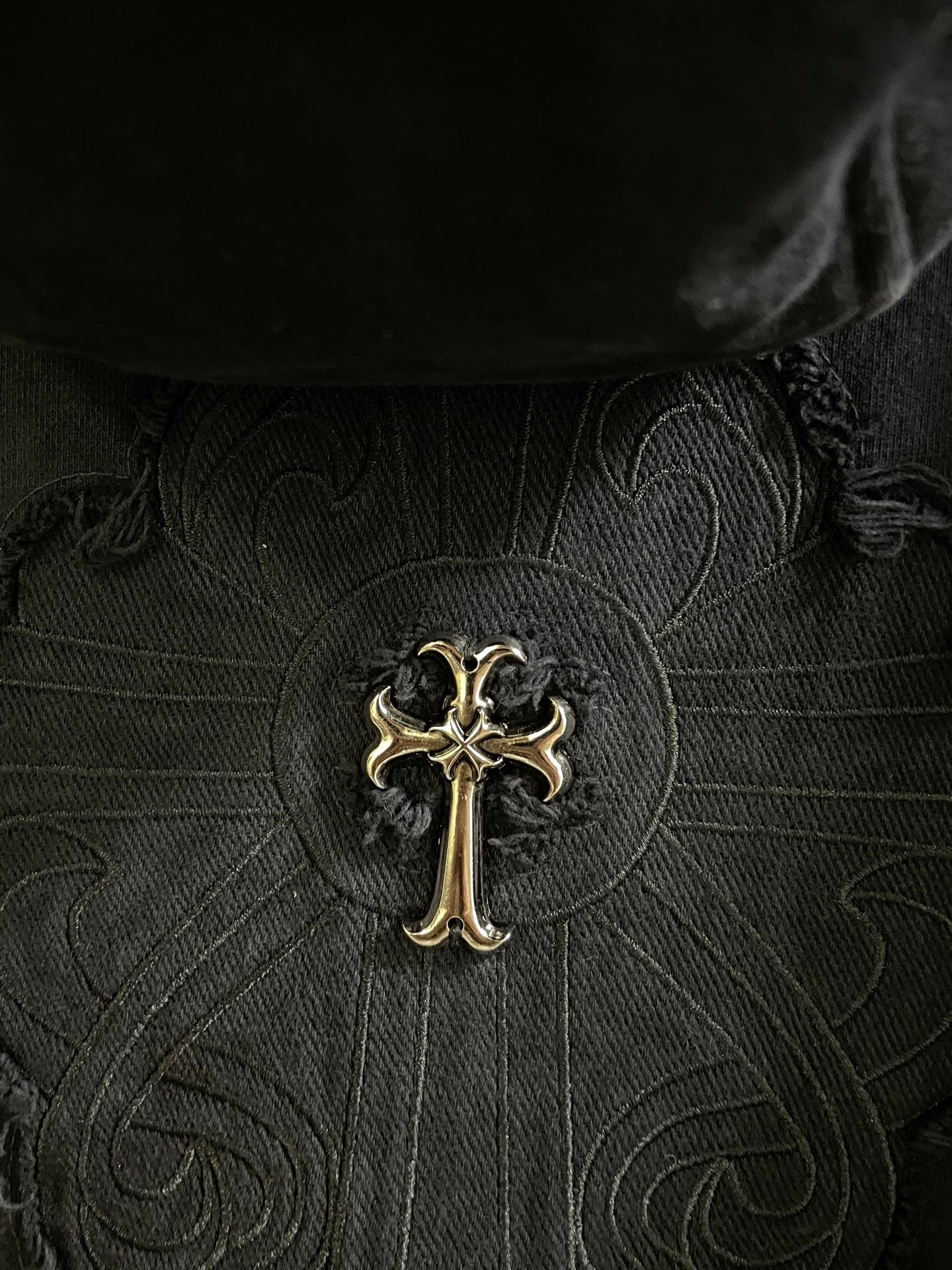 Close-up of dark embroidered cross emblem on patterned fabric center panel