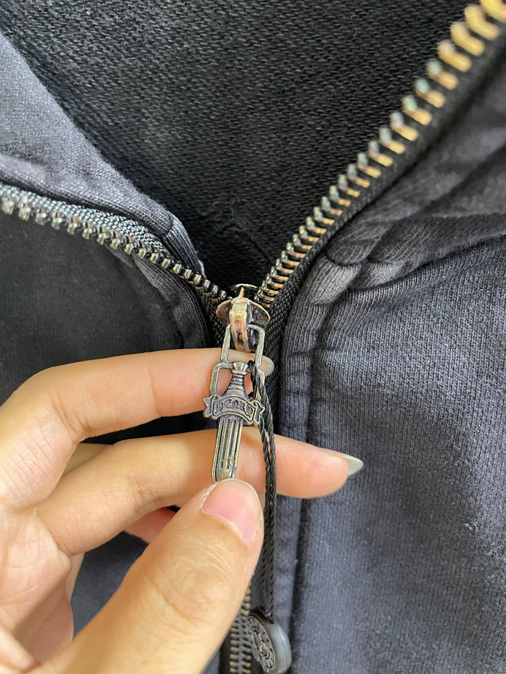 Close-up of zipper pull on dark hoodie with metal charm and engraved hardware
