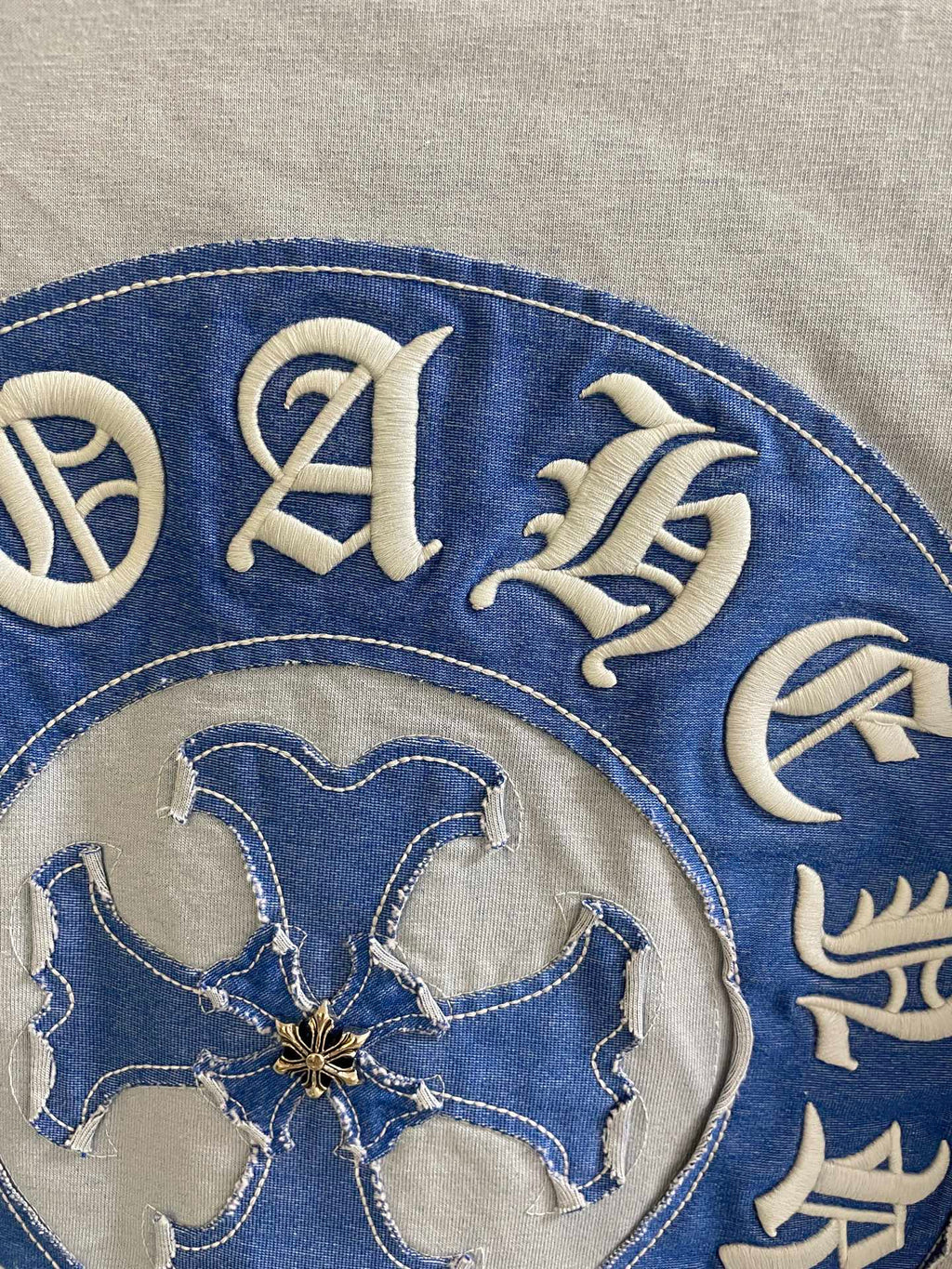 Blue circular crest on a light garment, detailed decorative letters and emblem.