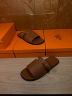 Brown leather slide sandals on orange shoe boxes, top straps with silver buckle hardware