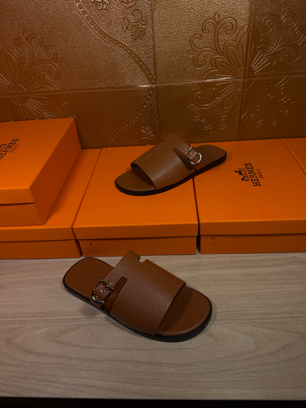 Brown leather slide sandals on orange shoe boxes, one pair with silver buckles