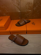 Brown leather slide sandals on orange shoe boxes, one pair with silver buckles