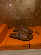 Brown leather slide sandals with wide strap and silver buckle detail, front view