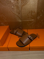 Brown leather slide sandals with silver buckle on two-strap upper, angled view