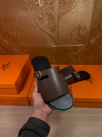 Dark brown leather slide sandals with silver buckles, close-up in hand