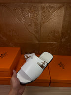 White slide sandals with double buckled straps and open toe, flat sole view