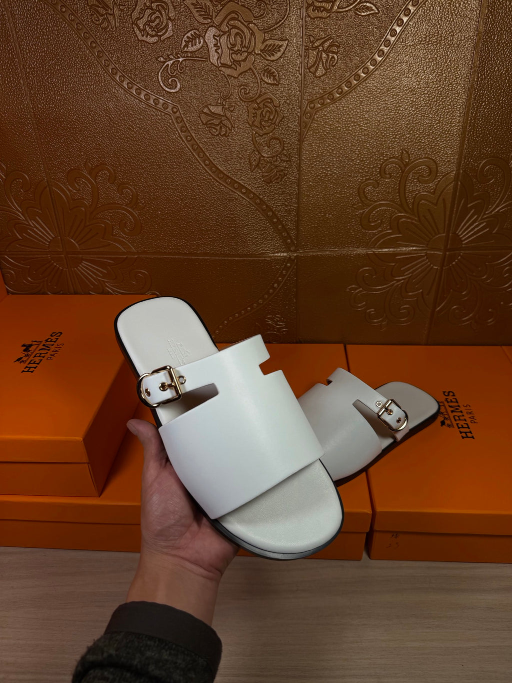 White slide sandal in hand, open toe with double straps and metal buckles