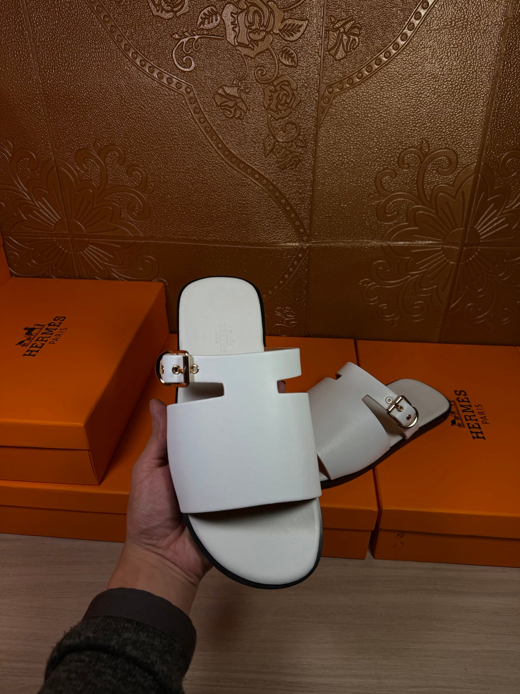 White slide sandals held up, open toe with double straps and metal buckles