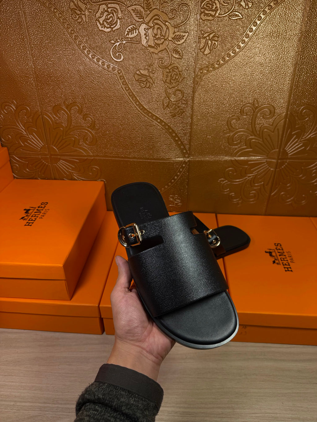 Black leather slide sandals with silver buckle, held up by hand