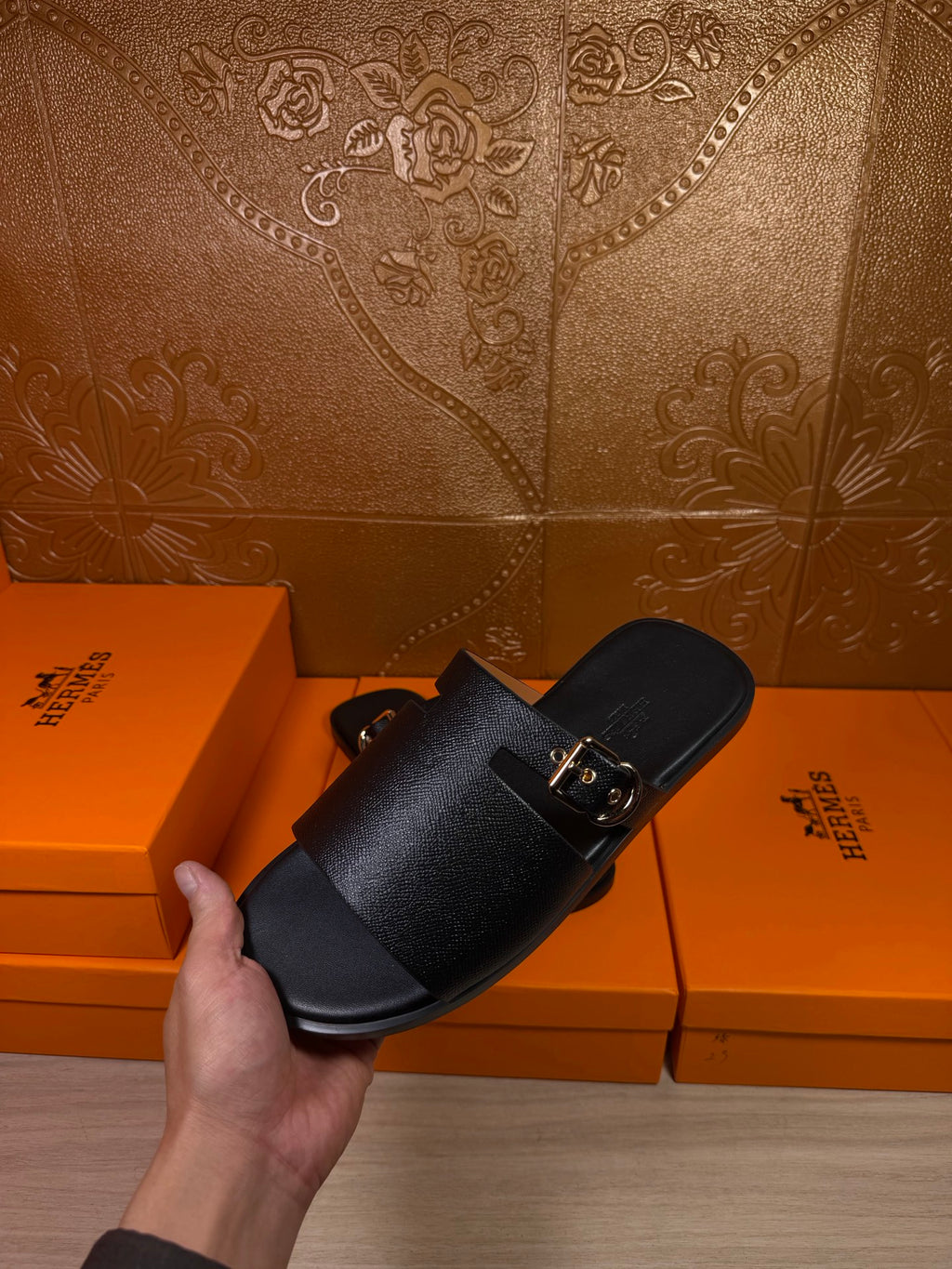 Black leather slide sandals with wide strap and silver buckle, hand model shot
