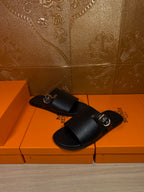 Black leather slide sandals with wide buckled strap, front 3/4 view