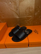 Black leather slide sandals with wide strap and silver buckle, pair view