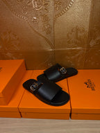 Black leather slide sandals with buckled strap and open toe, side view