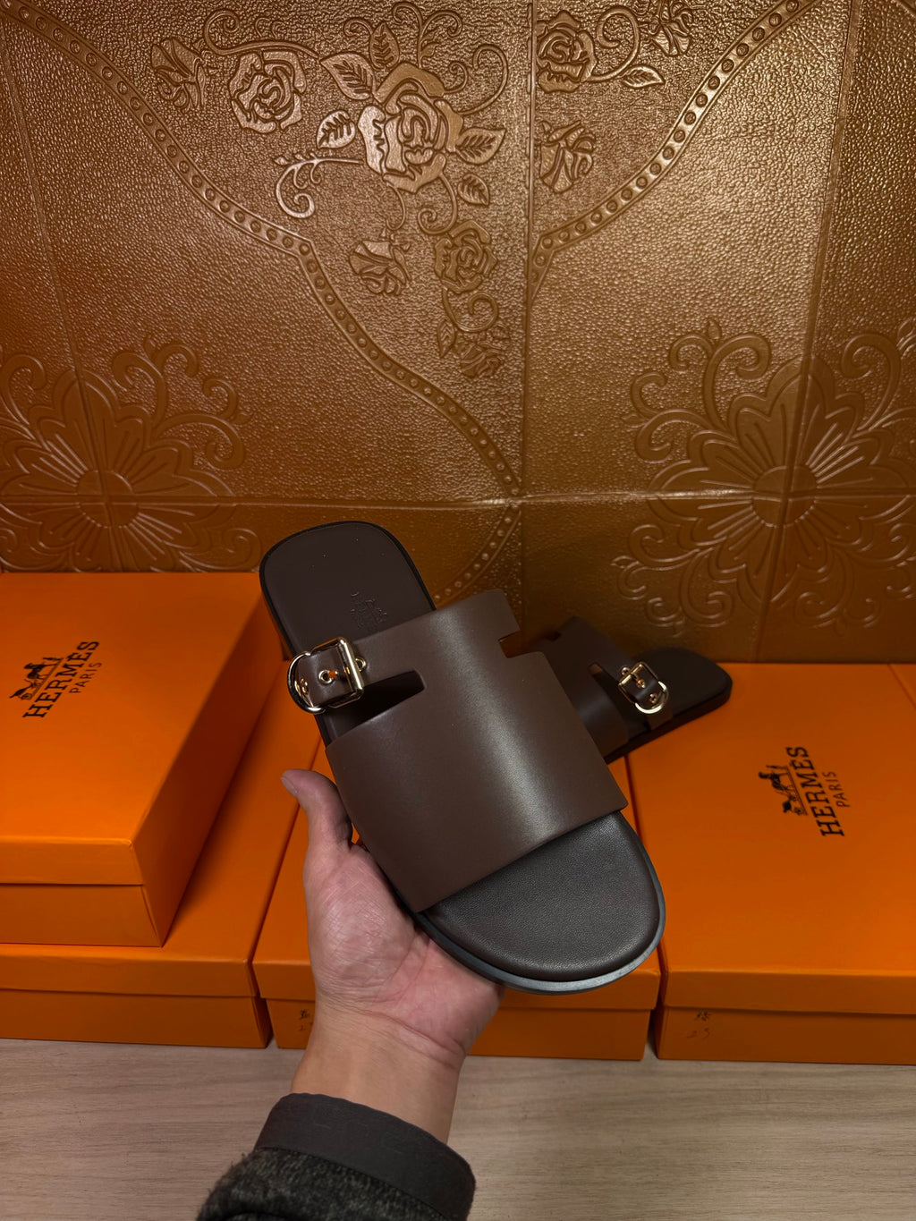 Hand holding Hermes dark leather slide sandal with buckle front strap