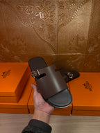 Hand holding Hermes dark leather slide sandal with buckle front strap