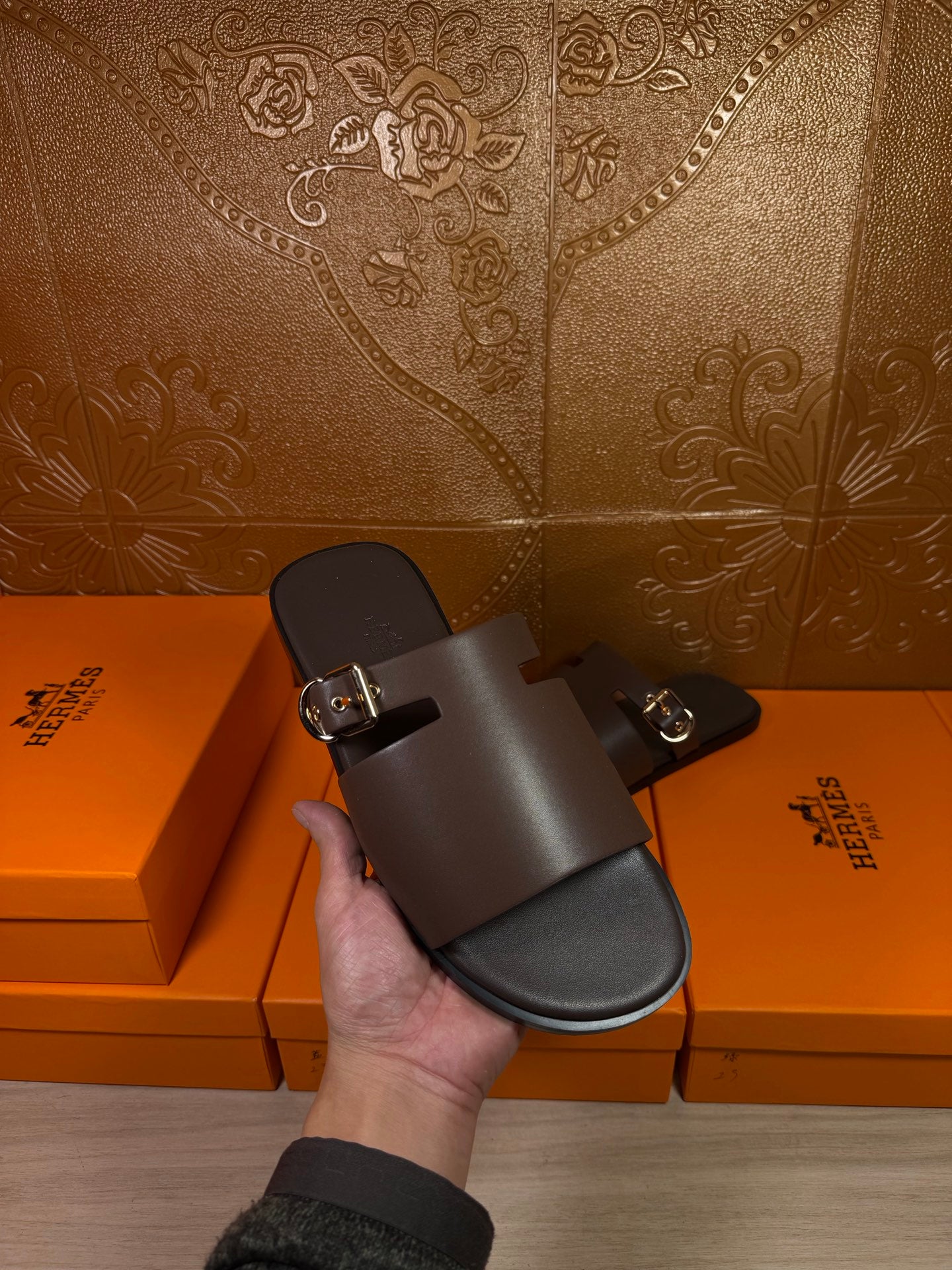 Hand holding Hermes dark leather slide sandal with buckle front strap