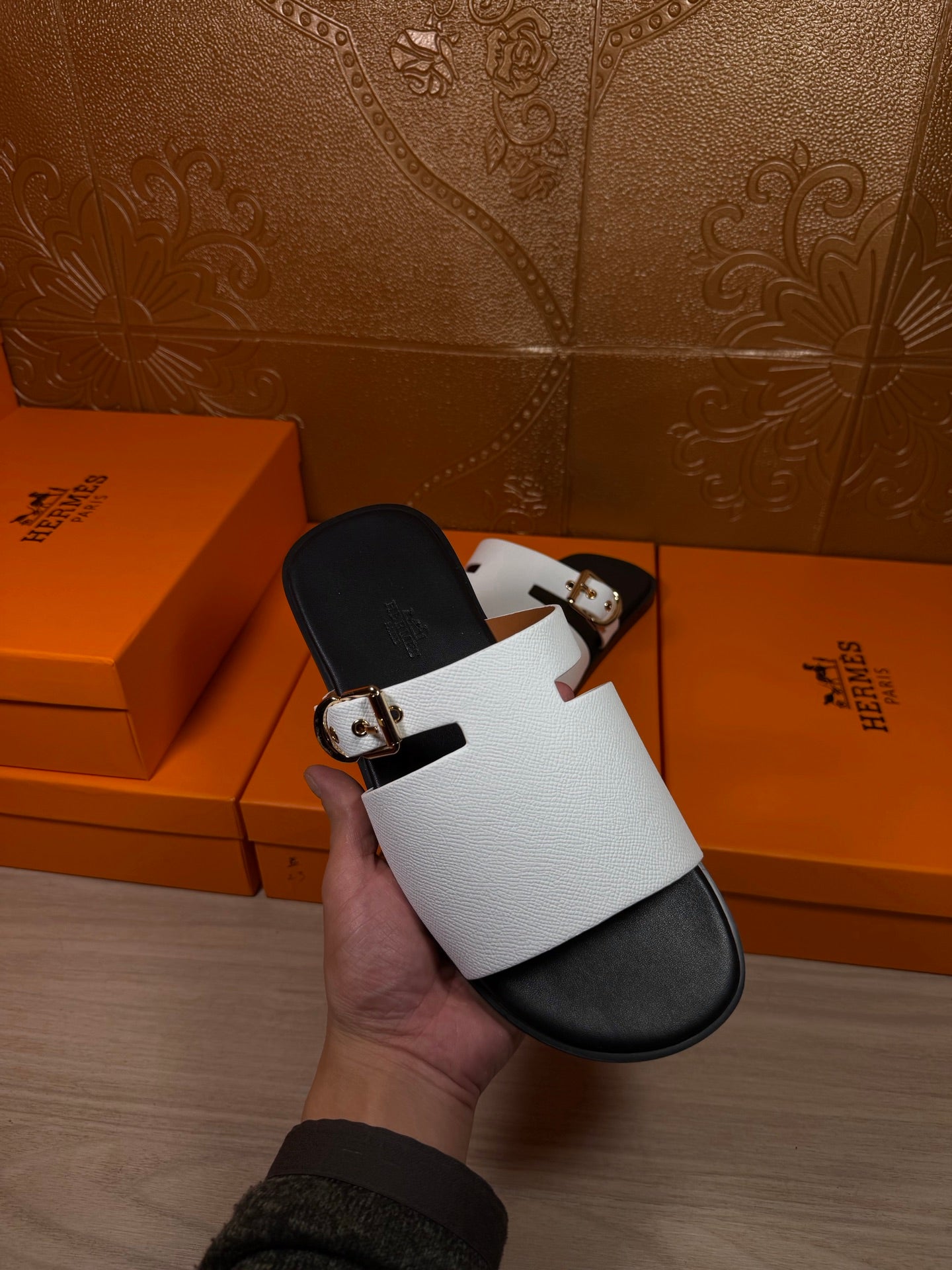 Hermes sandals being held: white strap with silver buckle over black footbed