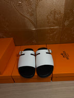 Hermes sandals with white straps and black footbeds, shown as a pair on a box