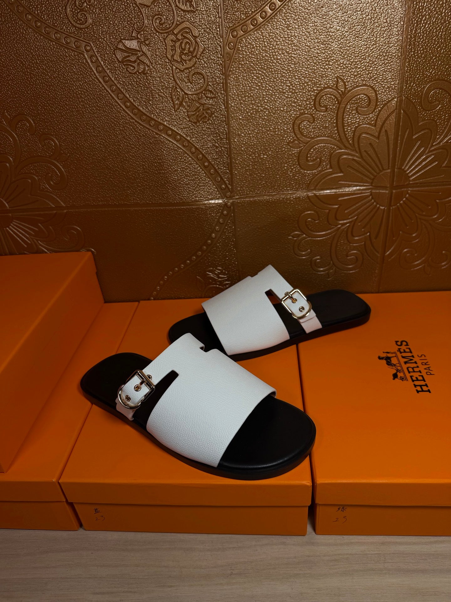 Hermes sandals with white upper and black footbeds, angled view resting on orange boxes