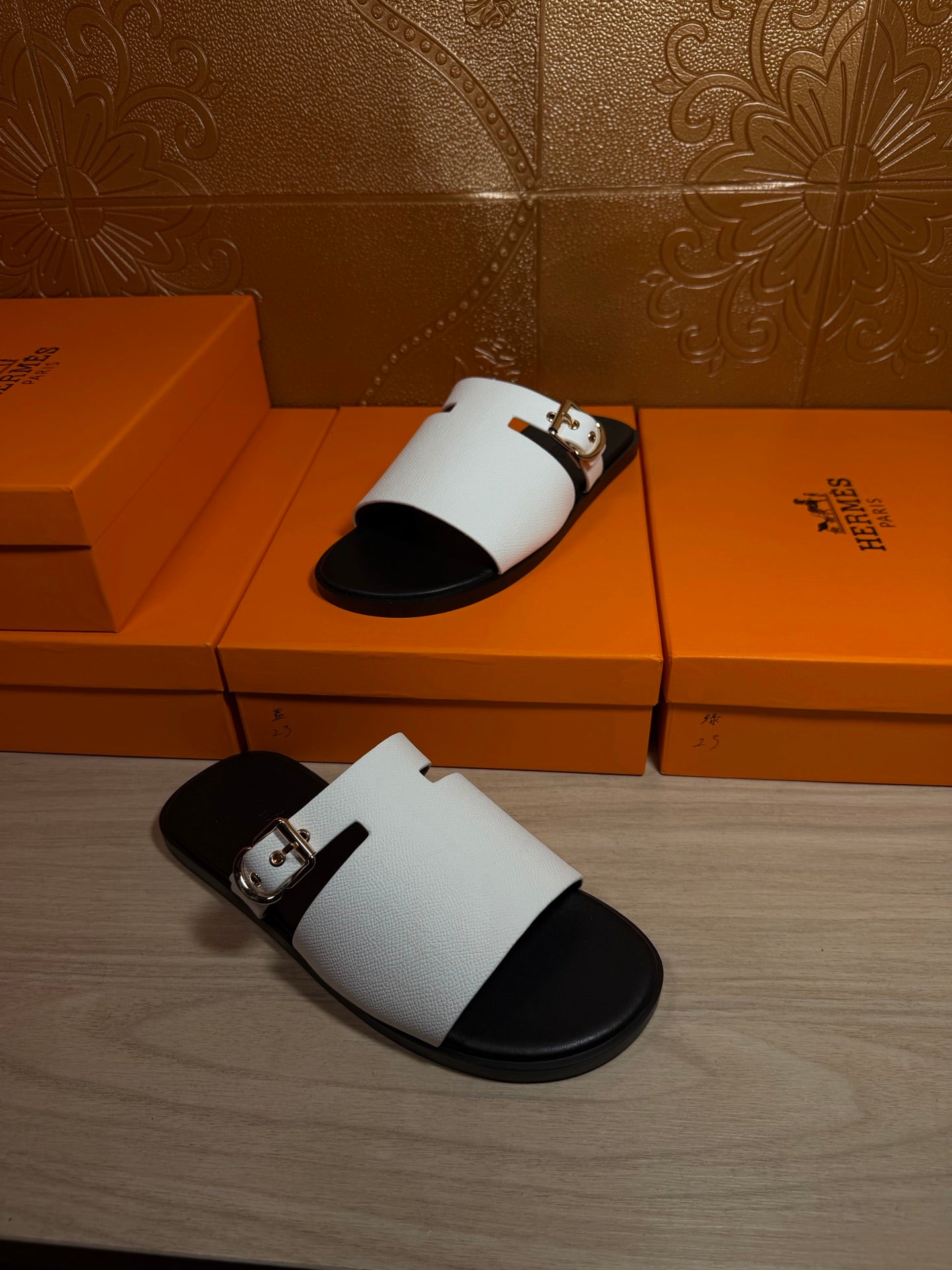 Hermes sandals with white slide straps and silver buckle, placed on orange shoeboxes