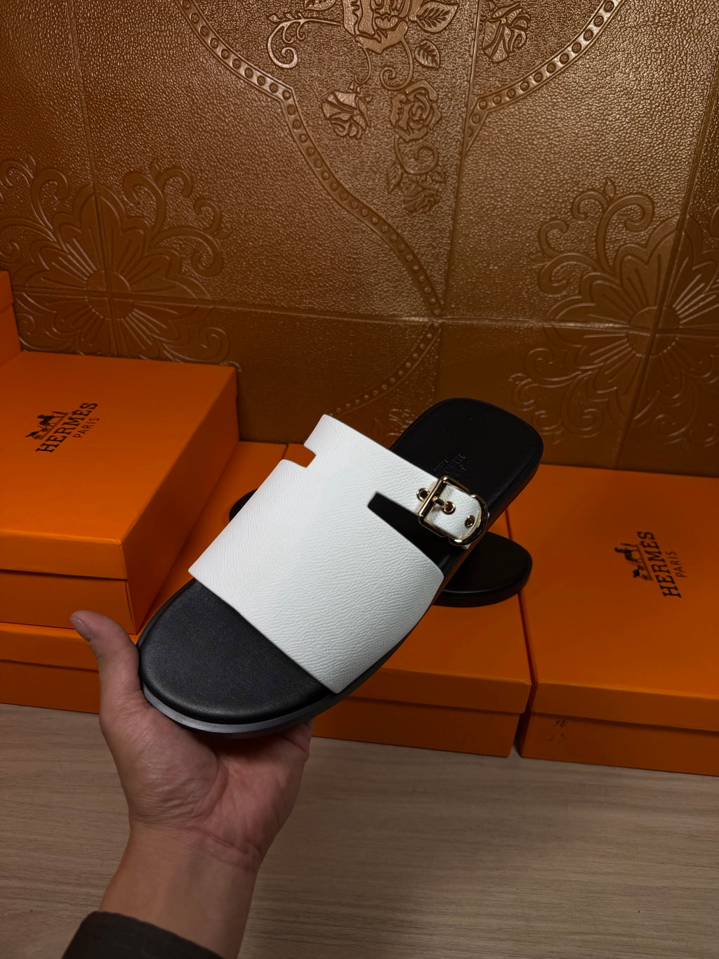 Hermes sandals held up: white strap with silver buckle and black sole footbed