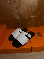 Hermes sandals with white slide straps and silver buckle hardware, side view on box