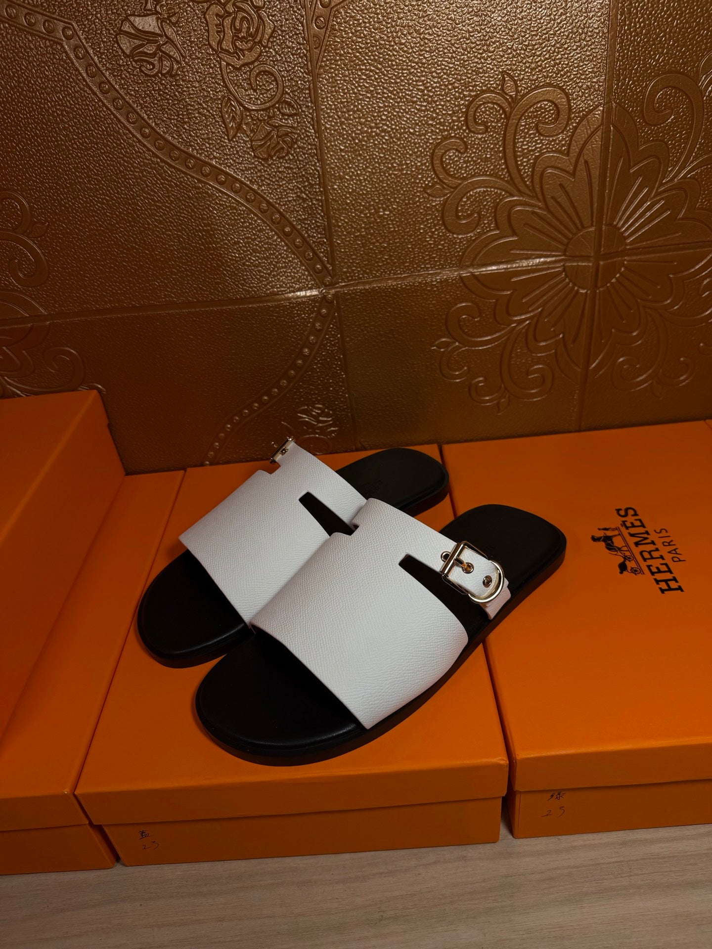 Hermes sandals with white slide straps and silver buckle hardware, side view on box