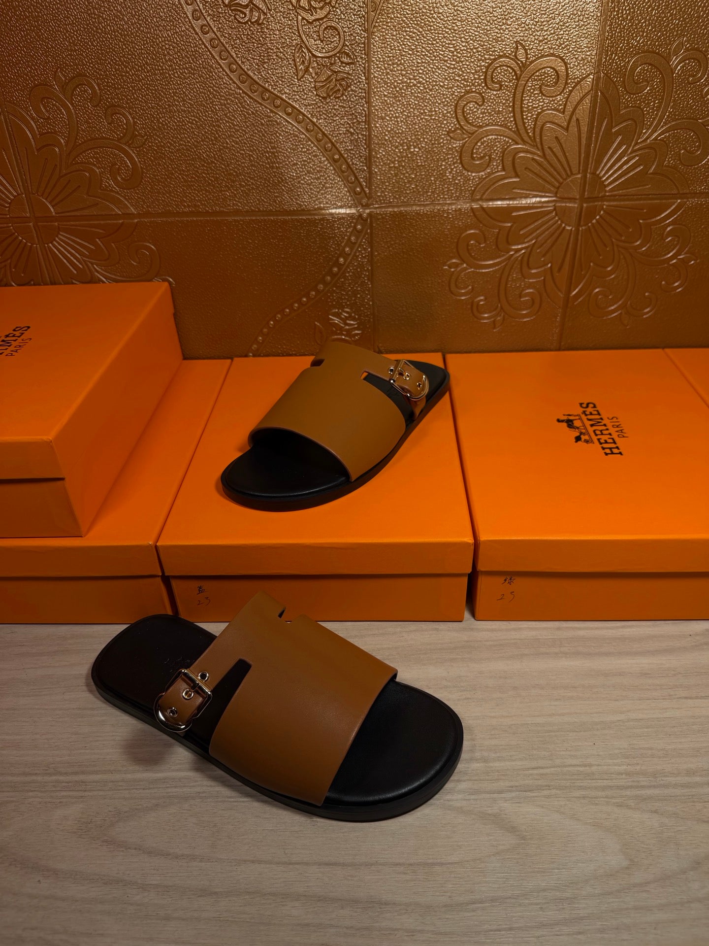 Leather slide sandal with tan upper and gold buckle, black sole and strap ends