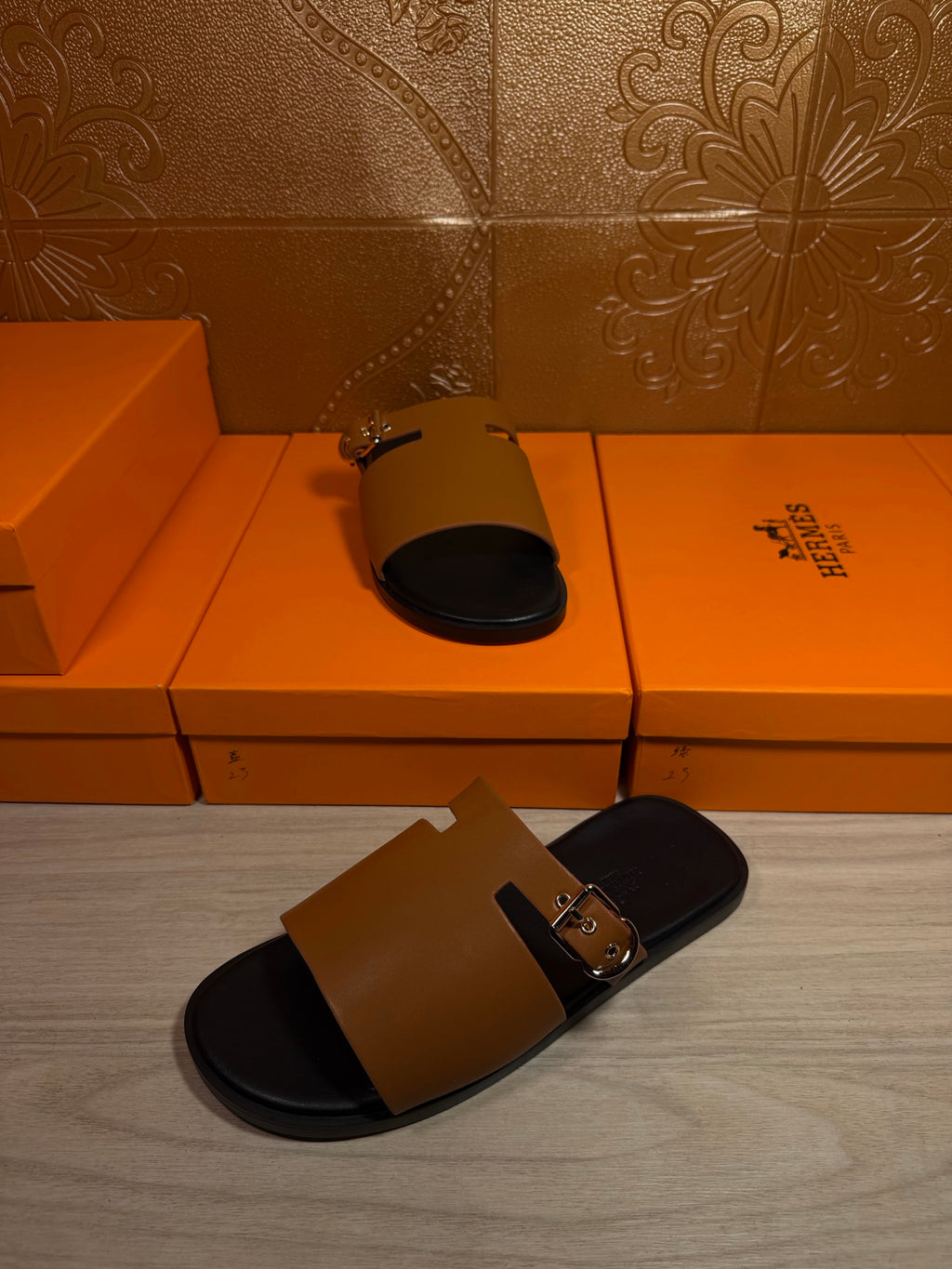 Leather slide sandal with tan strap and gold buckle over black footbed
