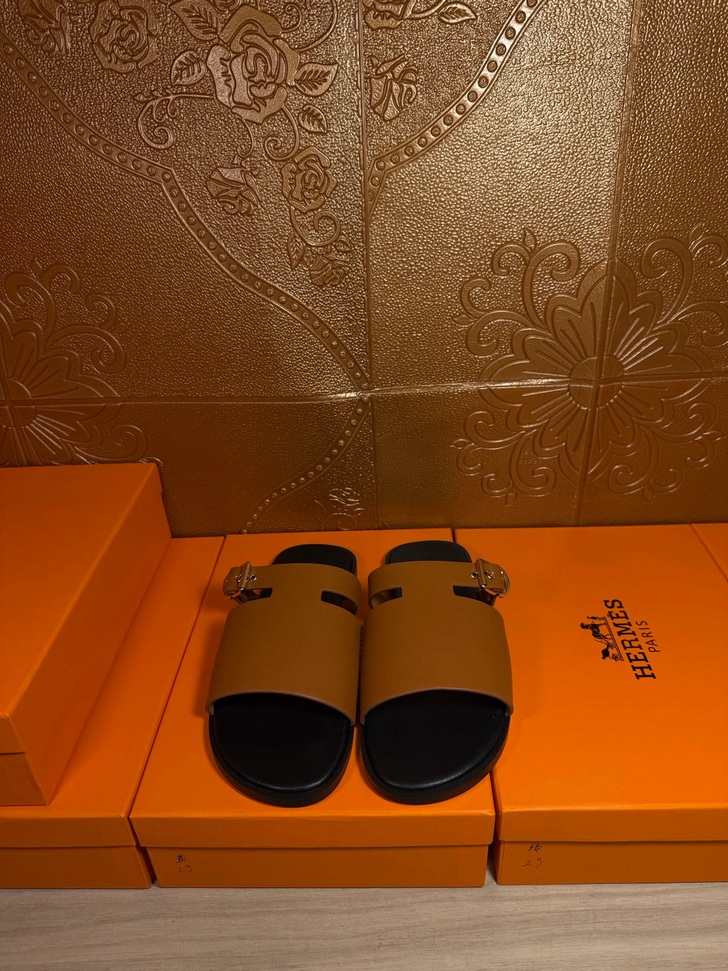 Leather slide sandals laid out, tan straps with gold buckles and black footbeds