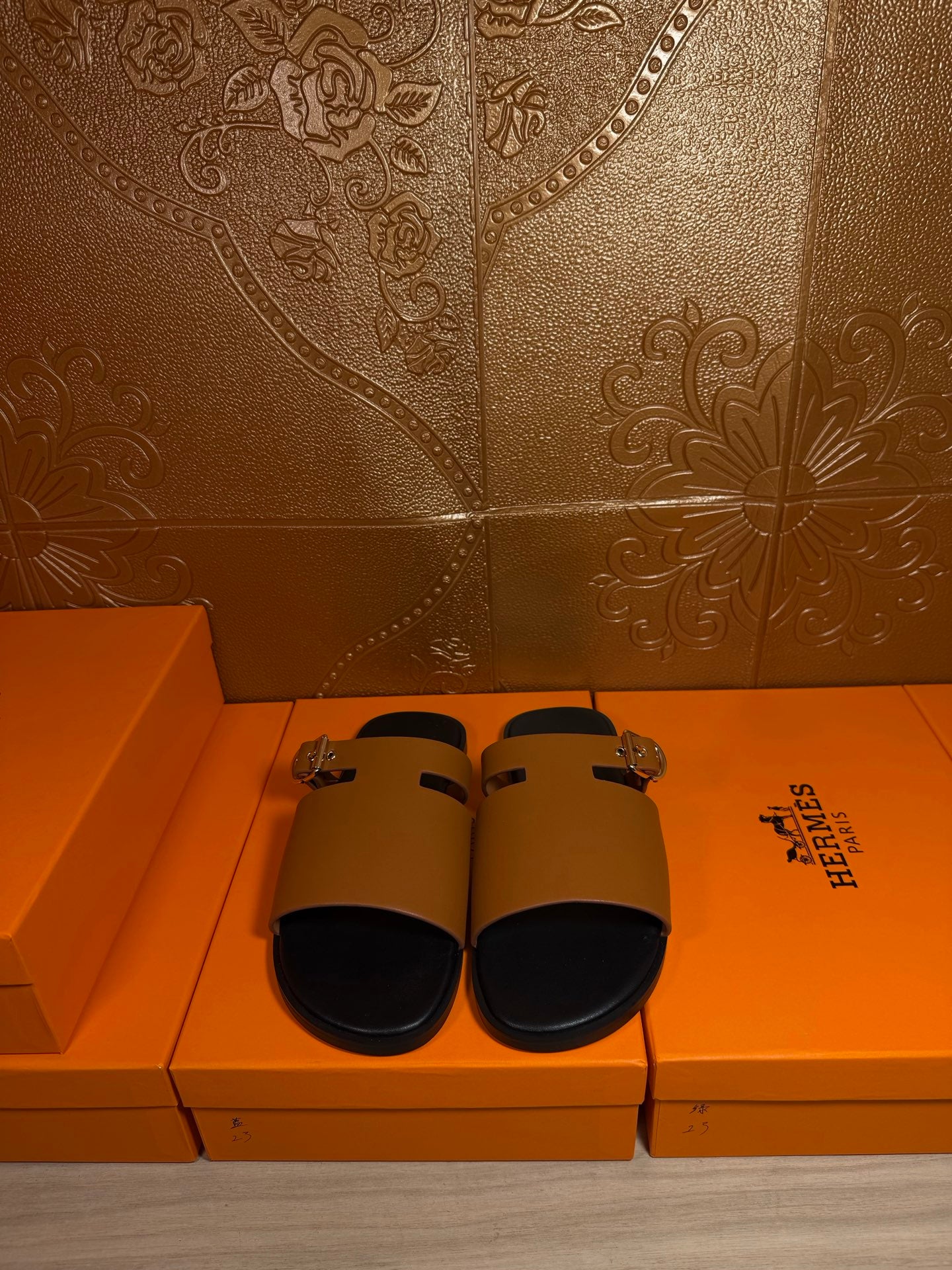 Leather slide sandals laid out, tan straps with gold buckles and black footbeds