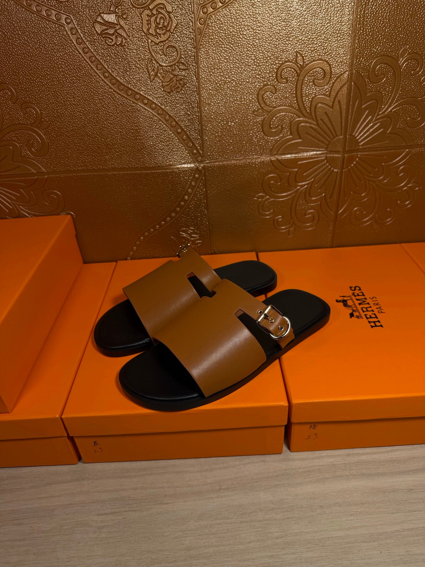 Leather slide sandals with tan uppers and gold buckles, black footbeds