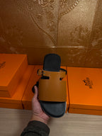 Hermes leather slide sandals with tan straps and gold buckle on black footbeds