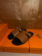 Hermes leather slide sandals with tan strap and gold buckle, black sole view