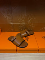 Hermes leather slide sandals with two silver buckles on wide straps, dark brown