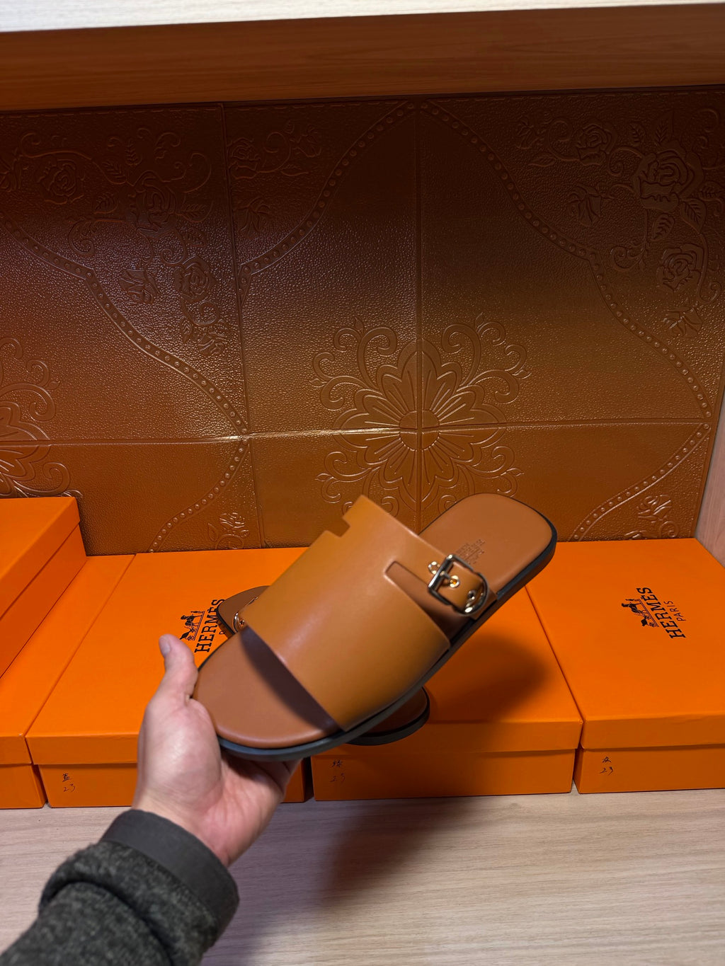 Leather Hermes slide sandal held in hand, wide strap with silver buckle, dark brown