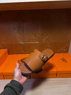 Leather Hermes slide sandal held in hand, wide strap with silver buckle, dark brown