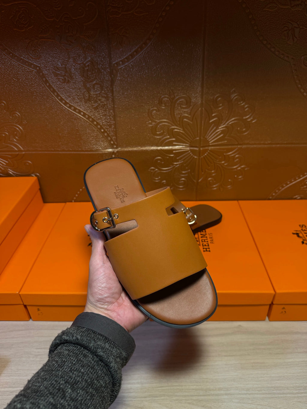 Hermes leather slide sandal in hand with silver buckle on wide strap, dark brown