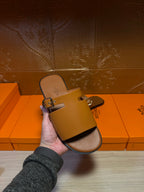Hermes leather slide sandal in hand with silver buckle on wide strap, dark brown