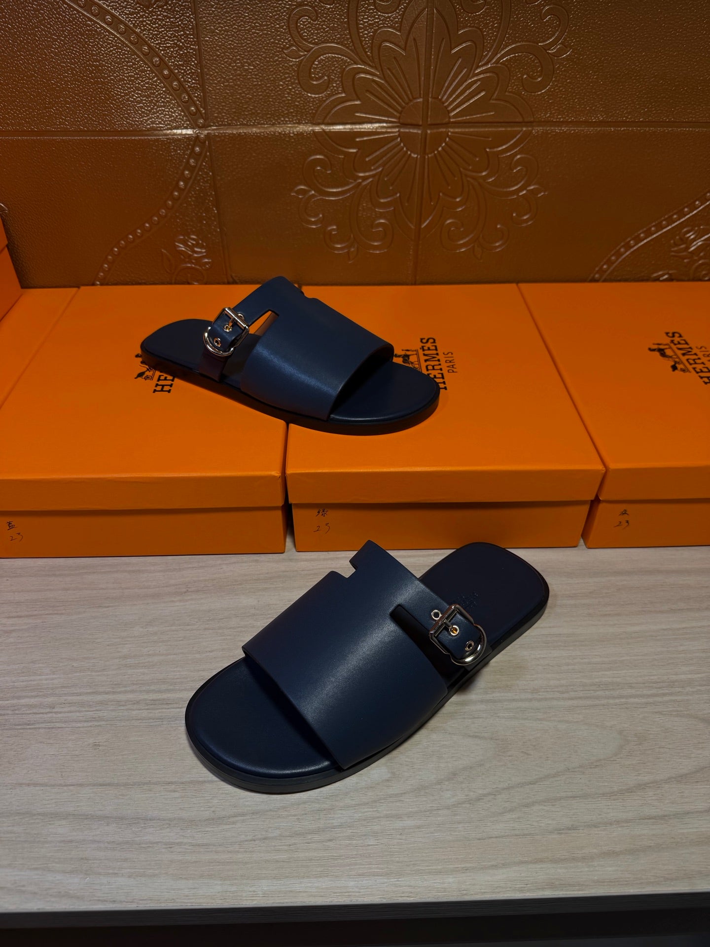 Hermes slide sandals pair, dark blue leather with gold buckles on two side straps.