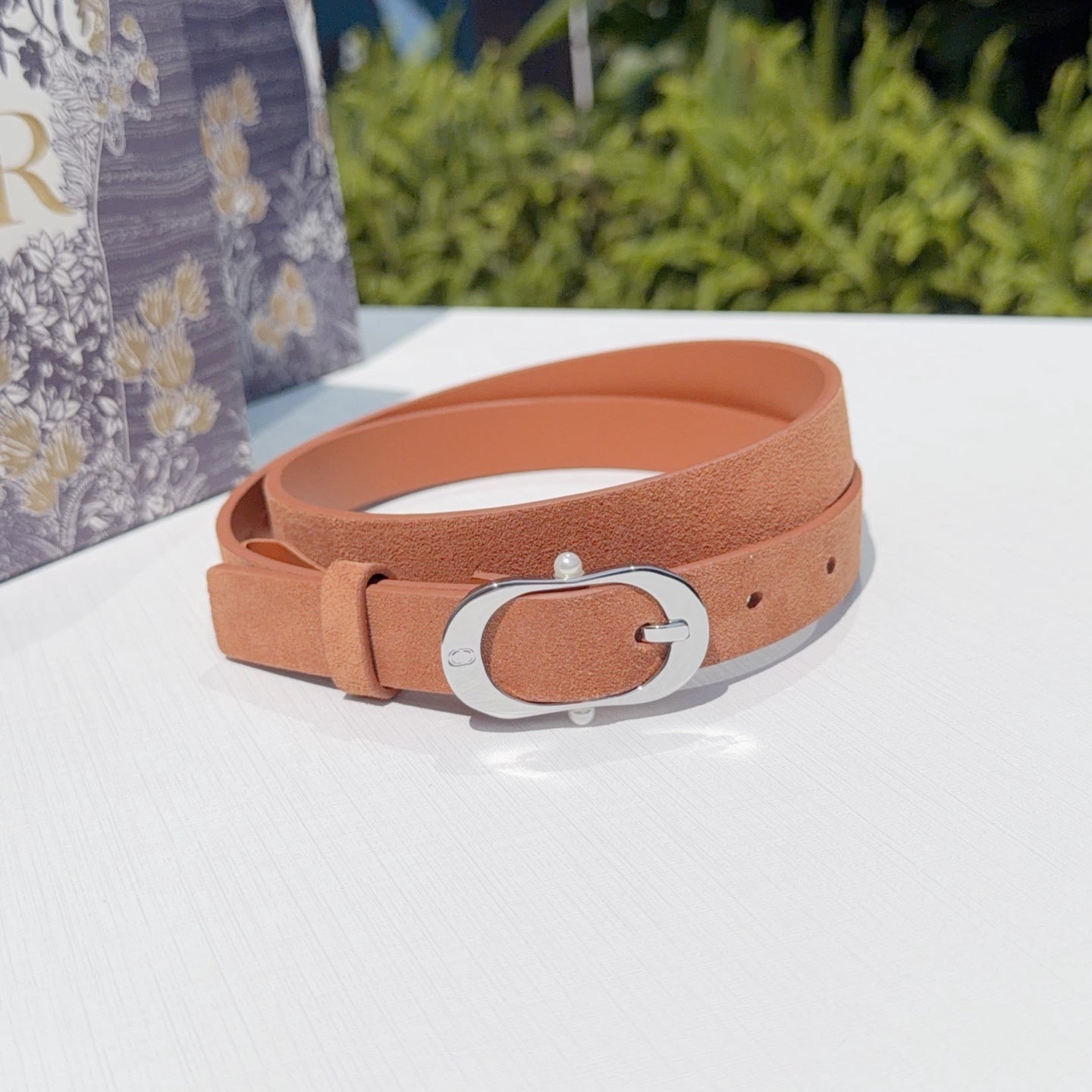 Dior belt, tan leather strap with silver oval buckle, angled view
