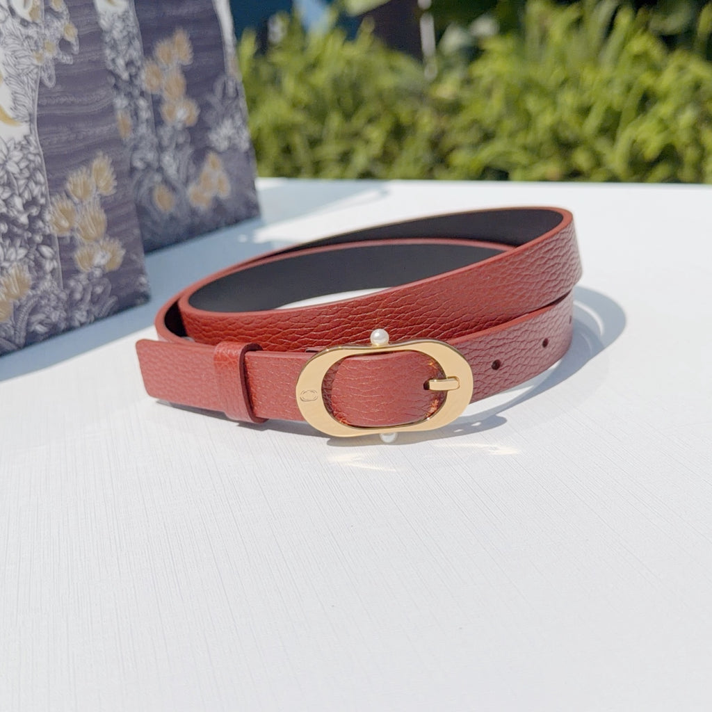 Coral leather belt with gold-tone circular buckle, shown coiled on a surface
