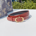 Coral leather belt with gold-tone circular buckle, shown coiled on a surface
