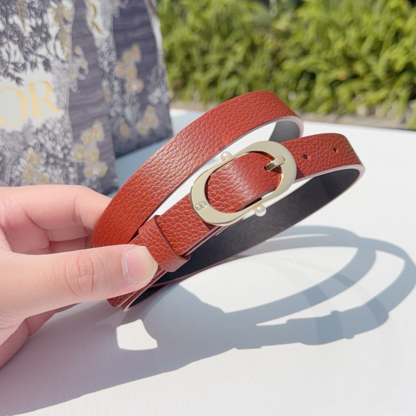 Coral leather belt with gold-tone buckle, held near the clasp in close-up