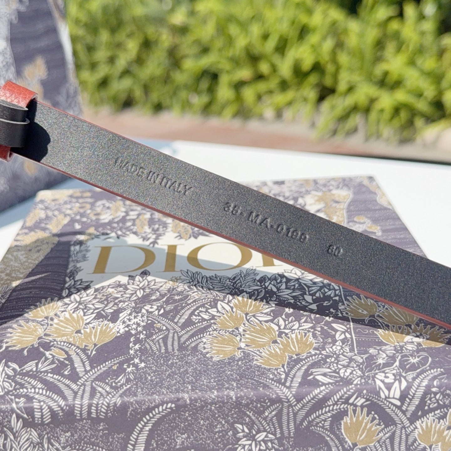 Grey leather belt underside with stamped text including 'Christian Dior' and numbers
