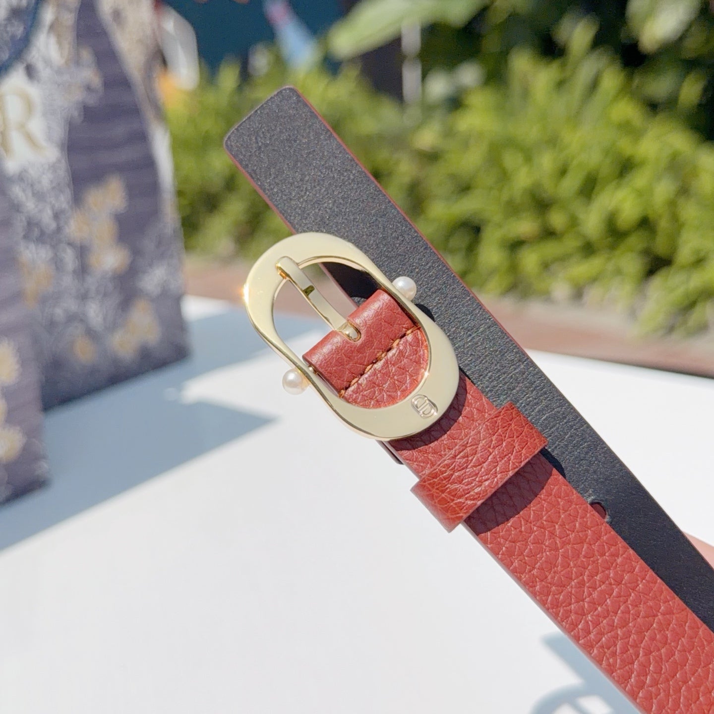 Coral leather belt detail with gold-tone buckle and perforation holes, angled