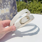 Leather belt held in hand, light gray strap with gold-tone buckle ring