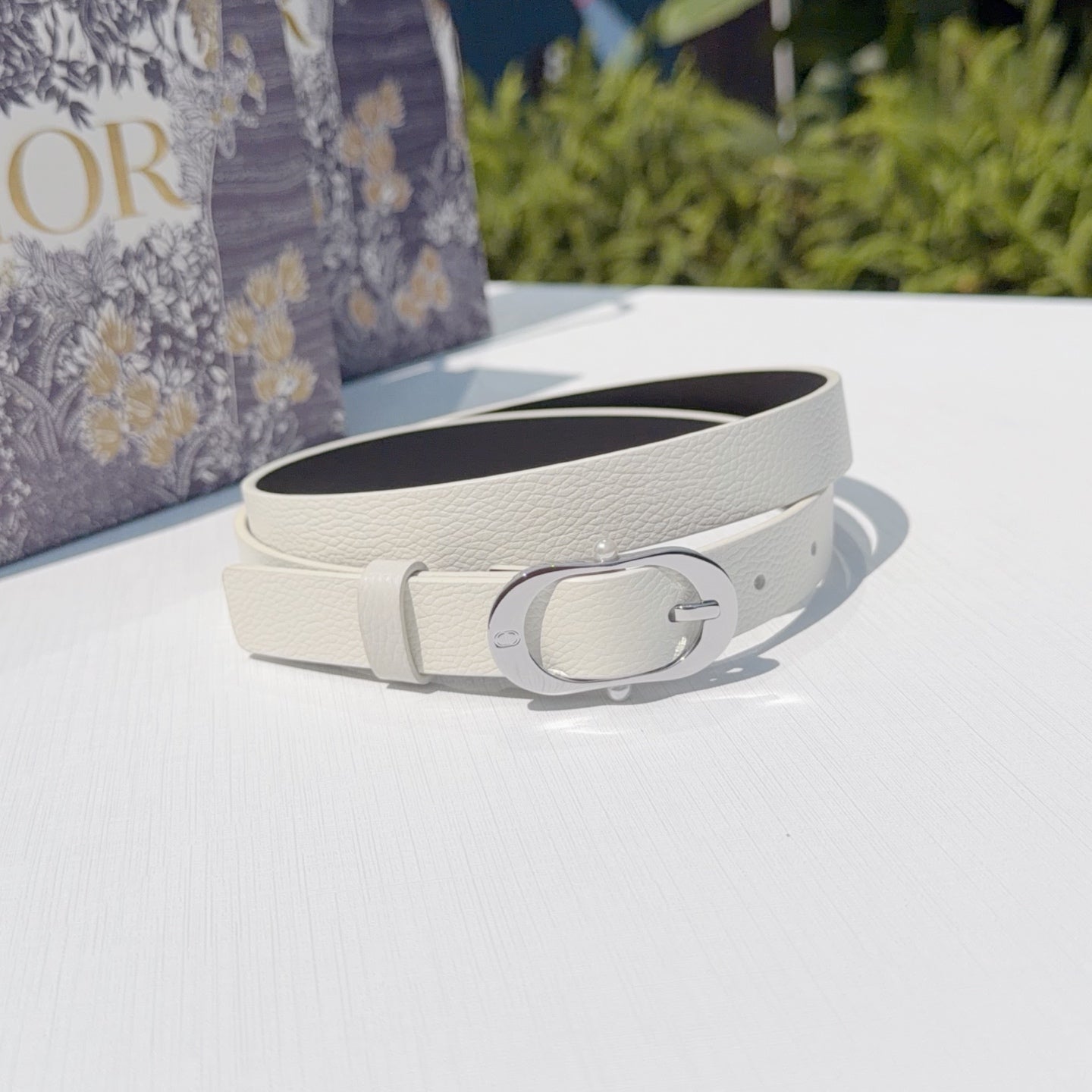 Dior belt with cream strap and silver oval buckle, laid flat